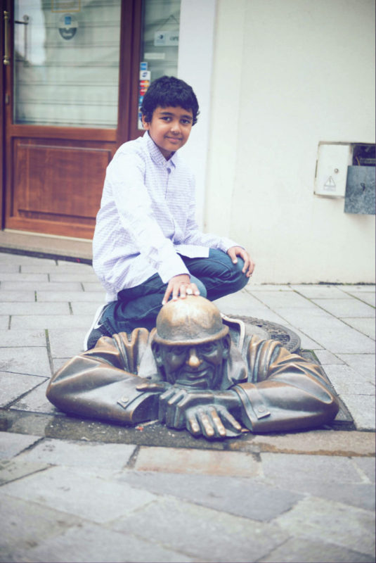 Asad, 9, poses with a popular statue of a man exiting a sewer in Bratislava